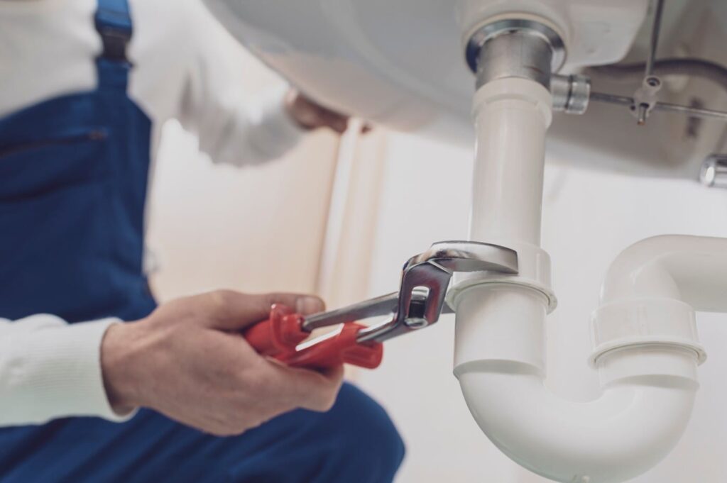 Plumber repairing a white drain pipe beneath a sink in Tucker