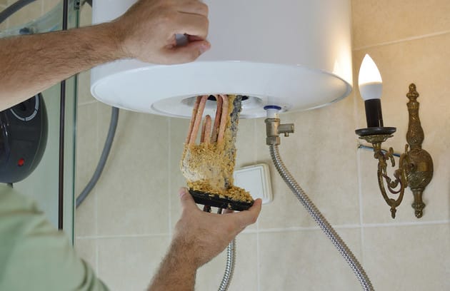 Technician removing mineral buildup from a water heater in Tucker